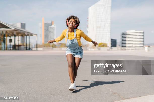 happy woman dancing on the street while enjoying listening music with wireless headphones. - musica y verano fotografías e imágenes de stock