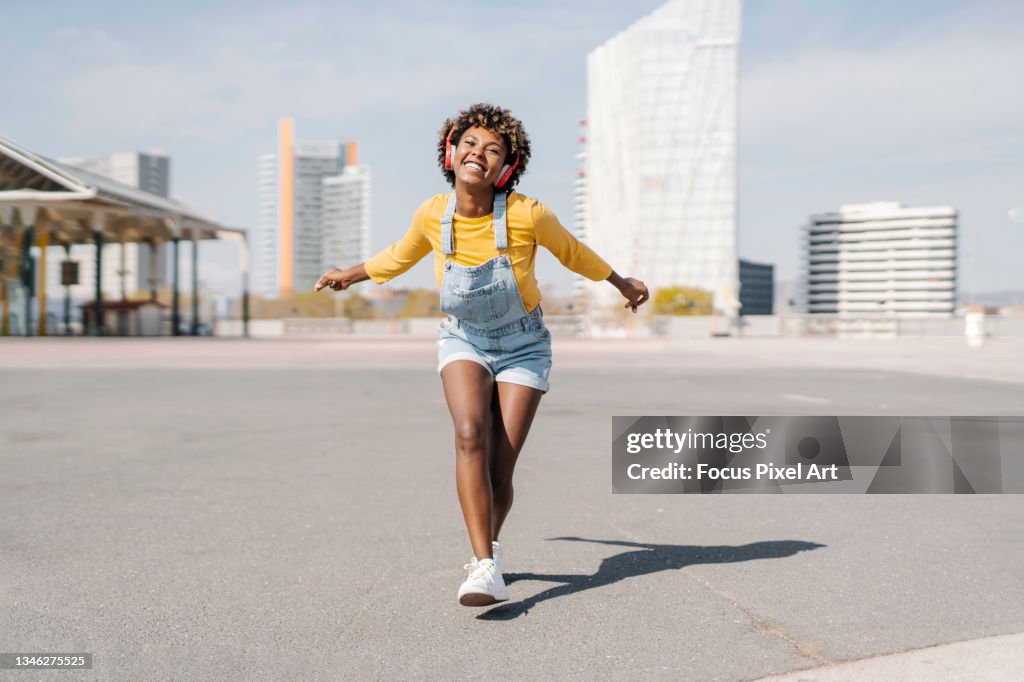 Happy woman dancing on the street while enjoying listening music with wireless headphones.
