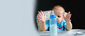 Banner tollder boy of 10 months drinking milk from a bottle in the kitchen at home. Baby food, dairy food concept.