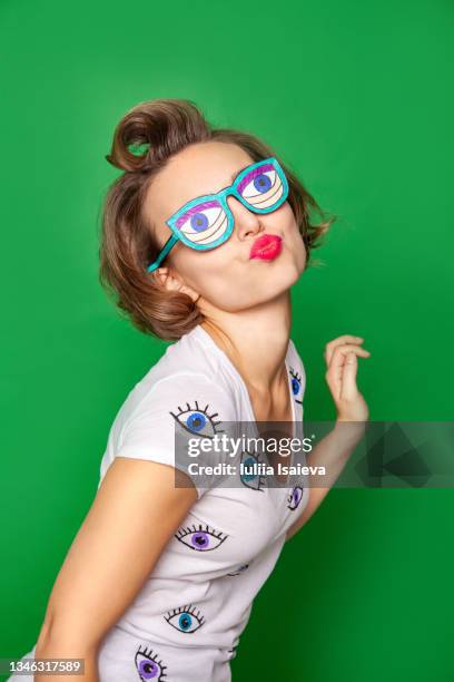 woman in funny glasses pouting lips against green background - quirky kissing foto e immagini stock