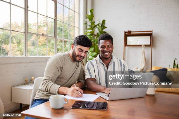 joven pareja gay sonriente que revisa las finanzas de su hogar juntos - finanzas domésticas fotografías e imágenes de stock