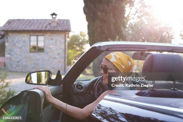 woman in driver's seat of a convertible car, closing the door - hair bun scarf woman stock pictures, royalty-free photos & images