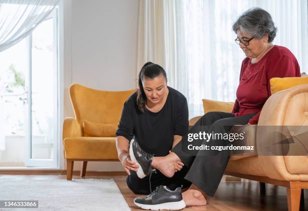 mujer ayudando a su anciana madre a usar zapatos en casa - asistencia de la comunidad fotografías e imágenes de stock