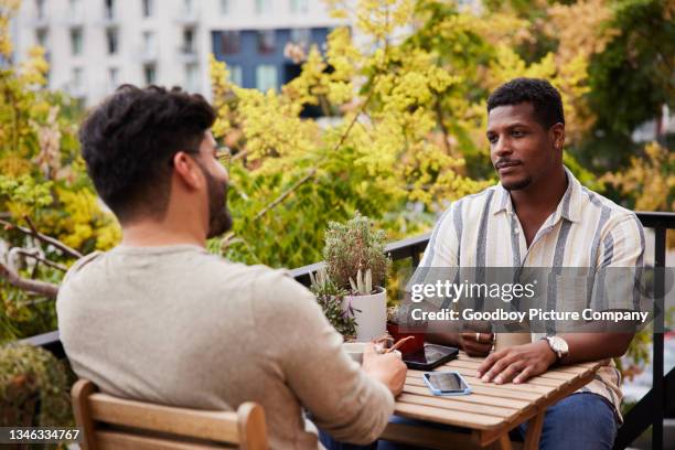 young gay couple talking over coffee on their apartment balcony - coffee on patio stock pictures, royalty-free photos & images