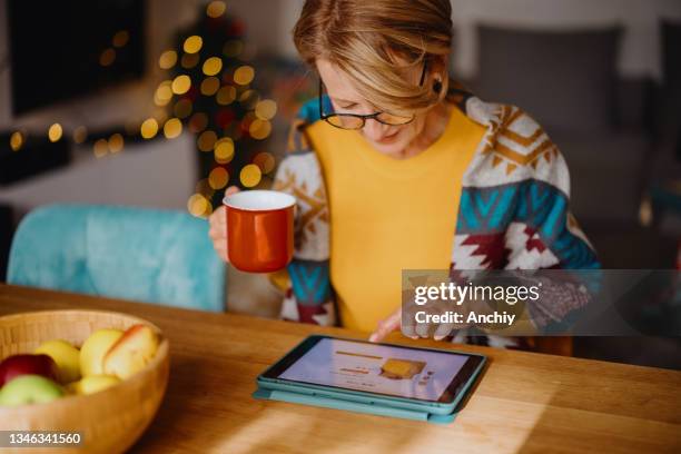 reife frau mit digitalem tablet für online-weihnachtseinkäufe - mature woman winter stock-fotos und bilder