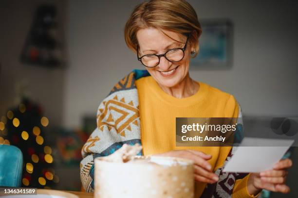 smiling woman unpacking parcel sitting at home - mature woman winter stockfoto's en -beelden