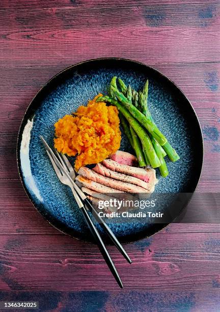 tuna steak with mashed sweet potatoes and steamed asparagus on a plate on wooden, red background - mashed potatoes stock-fotos und bilder