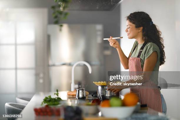 lächelnde frau, die beim kochen von spaghetti zum mittagessen genießt. - cooking kitchen stock-fotos und bilder