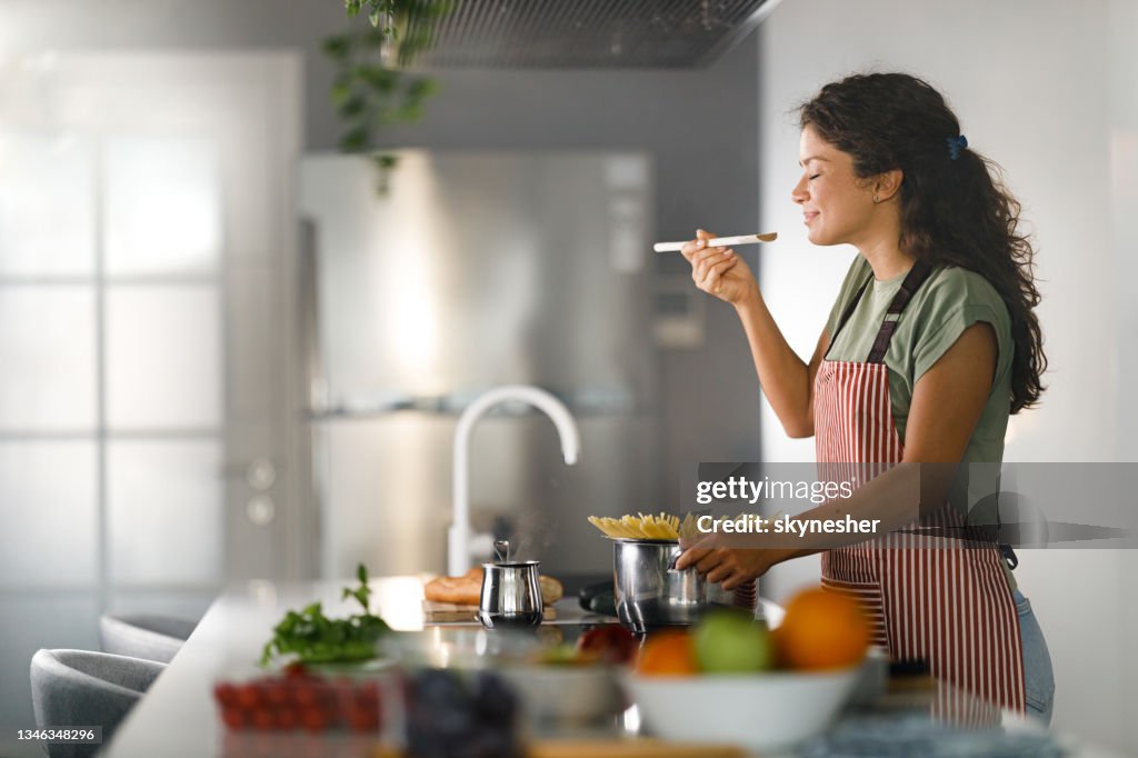 Smiling woman enjoying while cooking spaghetti for lunch.