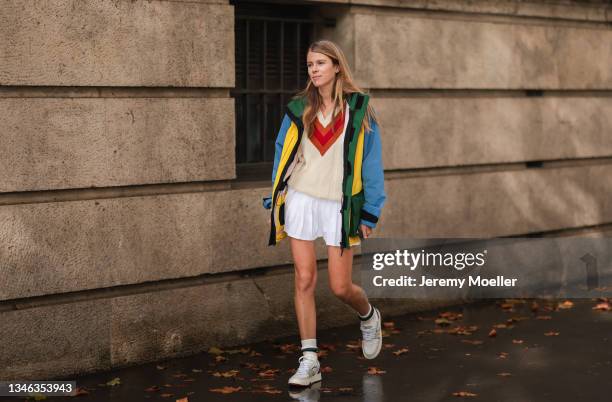 Fashion Week Guest wearing a colorful jacket, a beige and red pullover and a white skirt outside Lacoste Show on October 05, 2021 in Paris, France.