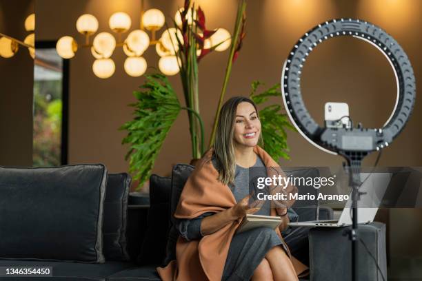 hermosa mujer realizando un directo desde casa mientras usa su anillo de luz para iluminarse a sí misma y a su teléfono celular para hacer el video - influencer fotografías e imágenes de stock