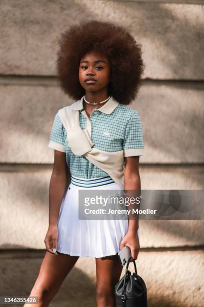 Fashion Week Guest wearing a blue shirt, a beige pullover and a white skirt outside Lacoste Show on October 05, 2021 in Paris, France.