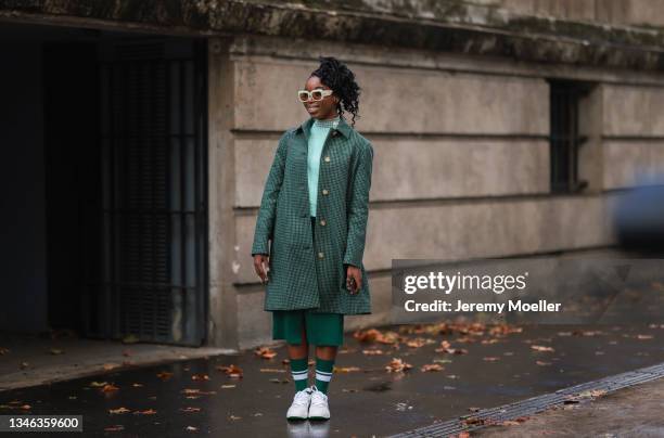 Fashion Week Guest wearing a green coat, a green dress and white sneakers outside Lacoste Show on October 05, 2021 in Paris, France.