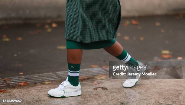 Fashion Week Guest wearing a green coat, a green dress and white sneakers outside Lacoste Show on October 05, 2021 in Paris, France.