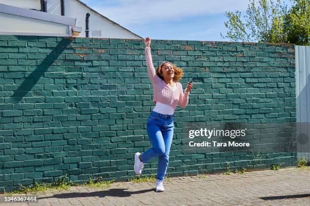 woman dancing in front of brick wall. - faust in die luft stoßen stock-fotos und bilder
