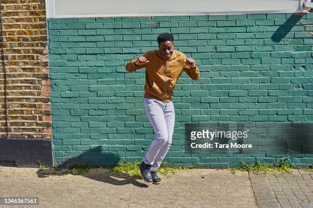man dancing in front of brick wall. - portrait of man smiling black jumper stock-fotos und bilder