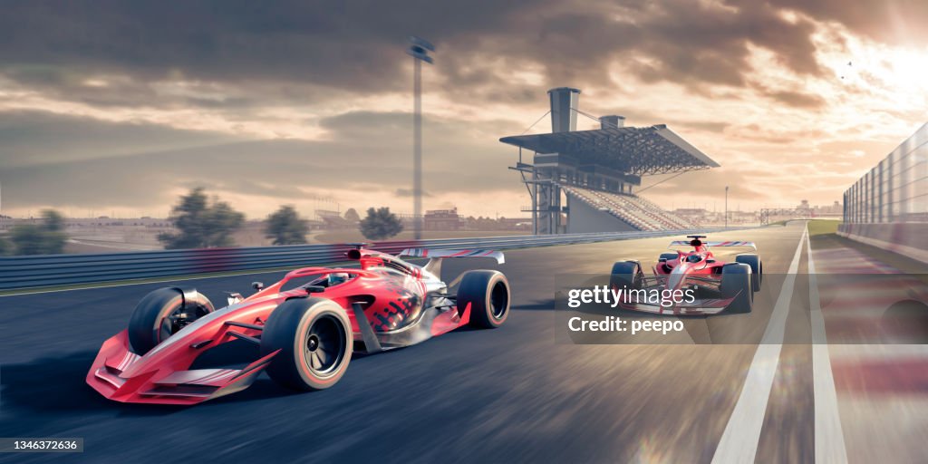 Dois carros de corrida vermelhos se movendo em alta velocidade ao longo do autódromo ao pôr do sol