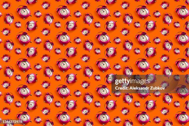 pink retro alarm clock on a red or orange background, in a row. the concept of the speed and rapidity of time and the flow of life. seamless pattern. - orange alarm clock stock pictures, royalty-free photos & images