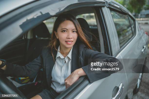 schöne asiatische fahrerin sitzt in einem auto und schaut in die kamera - anzug ausland stock-fotos und bilder
