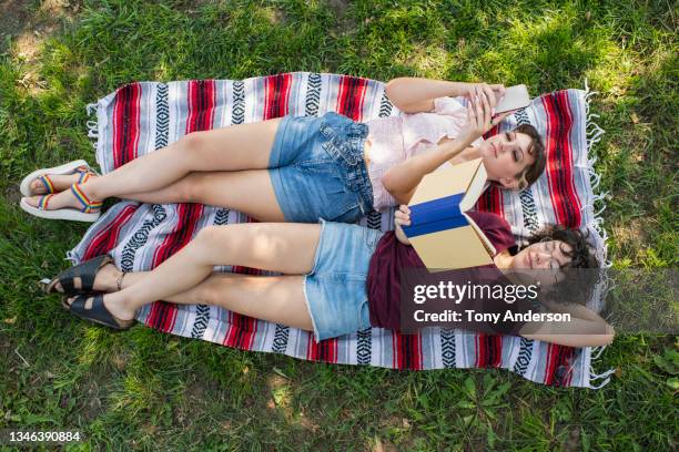 young female same sex couple on picnic blanket with phone and book - looking above stockfoto's en -beelden