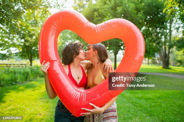 young female same sex couple kissing framed by large red inflatable heart - valentine's day holiday stock pictures, royalty-free photos & images