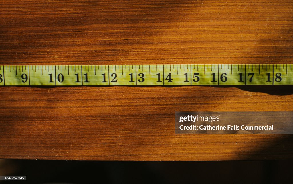 Simple image of a standard yellow tape measure on a wooden surface