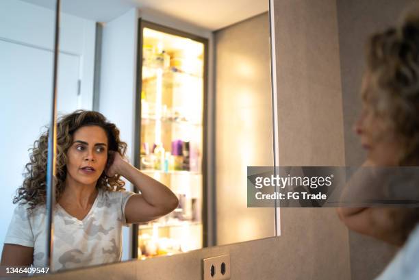 mature woman looking in the mirror styling her hair at home - standing mirror stock pictures, royalty-free photos & images