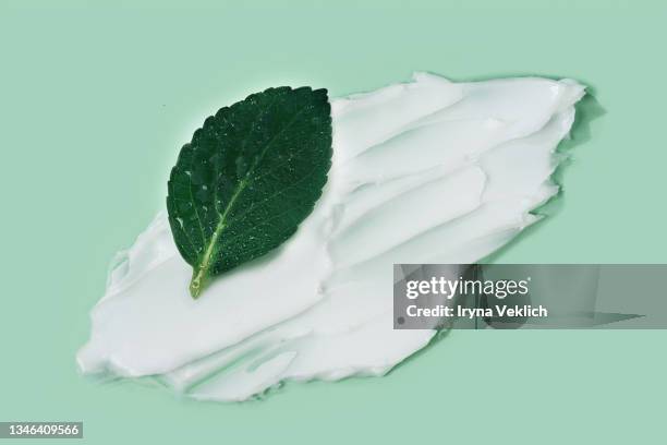 texture of white color moisturizing cream smudge and green leaf on pastel green color background. - skin care ingredients stock pictures, royalty-free photos & images