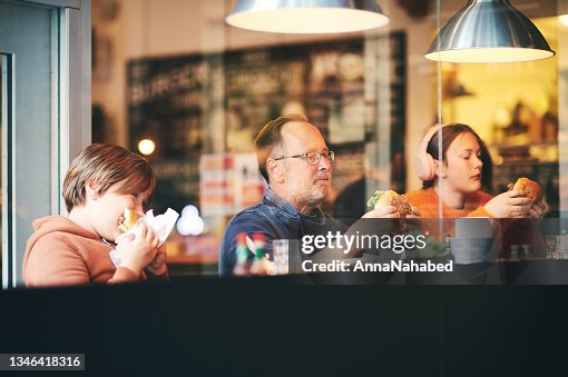 Family lunch, father with children eating hamburgers, in restaurant, sitting by the window Family lunch, father with children eating hamburgers, in restaurant, sitting by the window