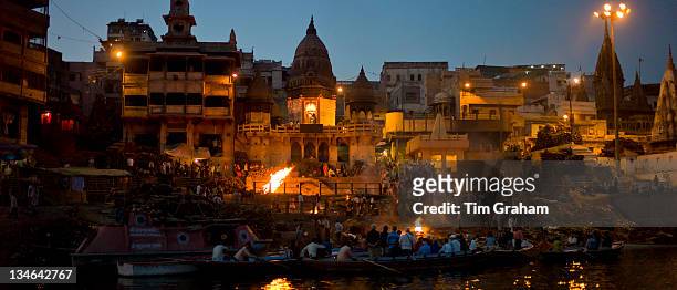 Tourists watch body bathed in River Ganges and traditional Hindu cremation on funeral pyre at Manikarnika Ghat in Holy City of Varanasi, Benares,...