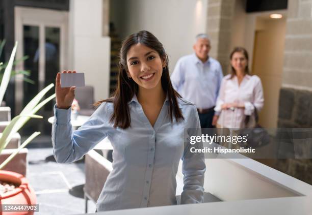 happy hotel receptionist holding a cardkey for her customers - loyalty cards stock pictures, royalty-free photos & images