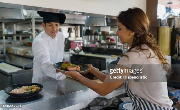 waitress receiving plates for service at a restaurant's kitchen - diner plates stock pictures, royalty-free photos & images