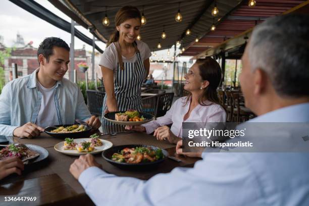レストランで幸せな家族のためにテーブルの上で食べ物を提供するウェイトレス - opening event ストックフォトと画像