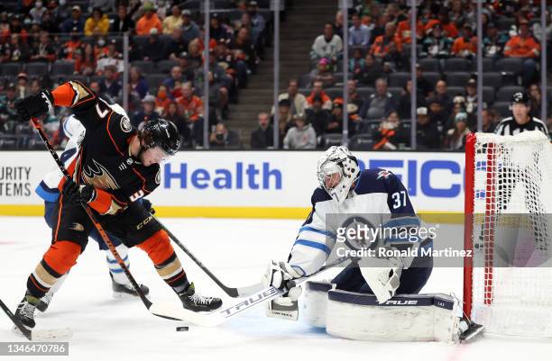 Mason McTavish of the Anaheim Ducks skates the puck against Connor Hellebuyck of the Winnipeg Jets in the second period at Honda Center on October...