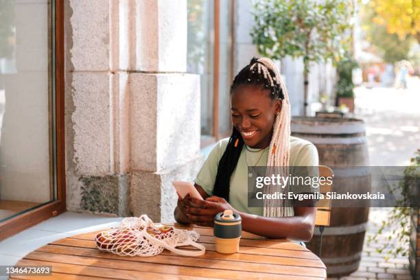 close-up portrait of young african woman using smartphone in street cafe. - scroll stock pictures, royalty-free photos & images