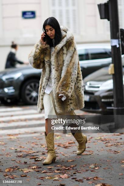 Guest wears a white shirt, a gold chain t-shirt, a brown and white oversized hoodie long coat, a white latte flowing skirt, beige shiny leather...