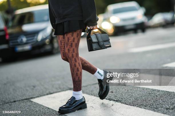 Guest wears a black sweater, a black pleated / accordion skirt, brown FF embroidered monogram pattern tights from Fendi, a black shiny leather...