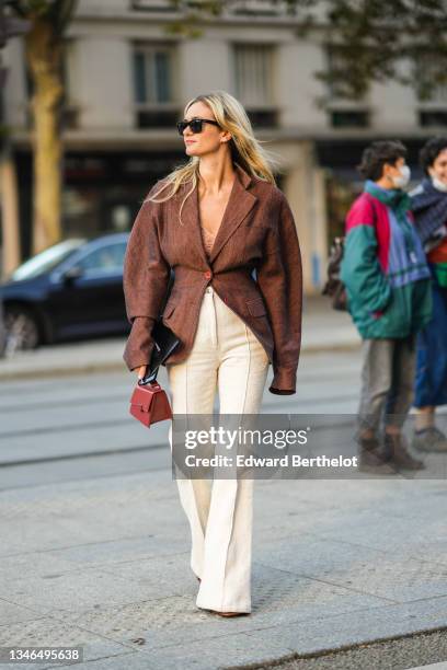 Anne-Laure Mais wears black sunglasses from Ray Ban, a beige braided wool V-neck t-shirt, a brown oversized blazer jacket, high waist beige tweed...