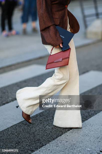 Anne-Laure Mais wears a brown oversized blazer jacket, high waist beige tweed flared pants, a red shiny leather handbag from Acne Studio, brown shiny...