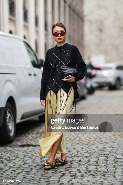Rosana Lai wears red sunglasses, gold earrings, gold pendant earrings, a black cut-out checkered pattern fringed pullover, a pale yellow satin long...