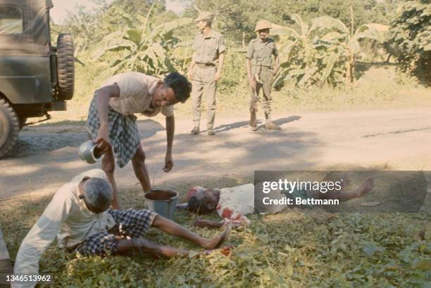 Man tends to two wounded people on a roadside, with soldiers in the background, close to the border with East Pakistan following shelling by...