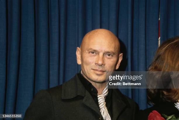 Russian-American actor Yul Brynner , wearing a grey overcoat over a black shirt and a black-and-white cravat, on his arrival in New York City, New...