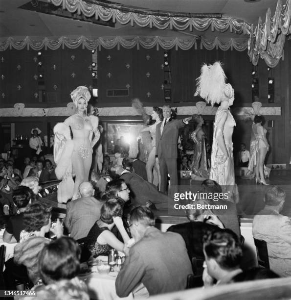 Scantily-clad female dancers, with feathered headdresses, on a catwalk for the entertainment of the club's patrons during the floor show at the Latin...