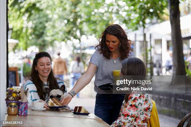 waitress serving drinks to two female customers - coffee break party photos et images de collection