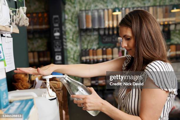 a women filling up at glass bottle in a refill shop - laundry-detergent-containers stock pictures, royalty-free photos & images