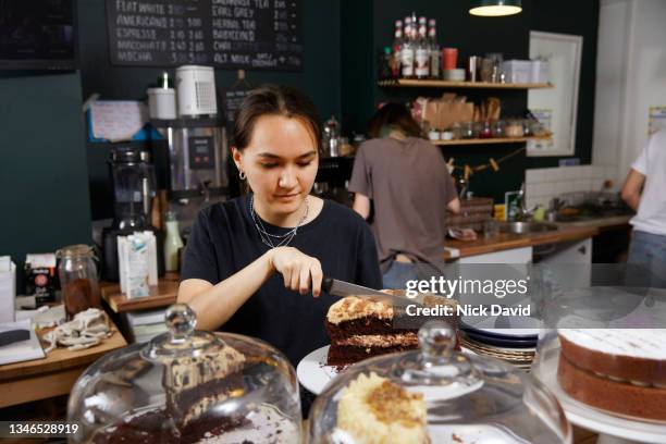 a waitress in a cafe cutting a slice of cake - barista stockfoto's en -beelden