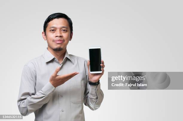 asian muslim young man showing smartphone with blank screen - handsome muslim men stock pictures, royalty-free photos & images