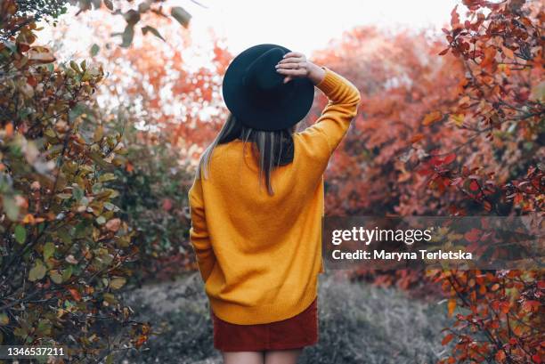 a girl stands with her back in a hat on nature in autumn. - goldene jacke stock-fotos und bilder