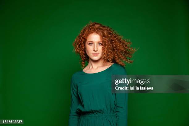 confident woman with flying red hair on green background - vrouw staat in mooie jurk stockfoto's en -beelden