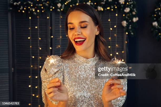 happy beautiful woman holding festive sparkler among christmas night - christmas party dress stock pictures, royalty-free photos & images